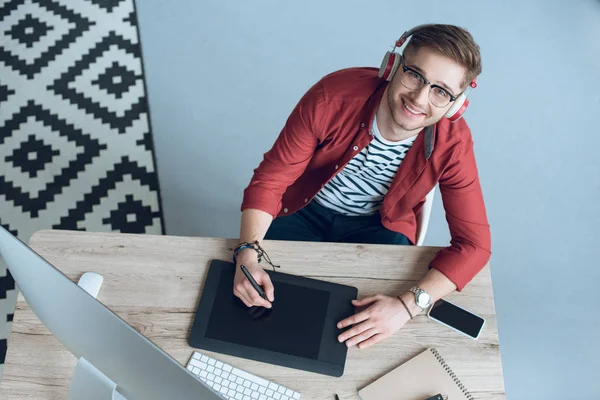 Sorrindo homem desenho com tablet gráfico na mesa com computador em casa escritório — Fotografia de Stock