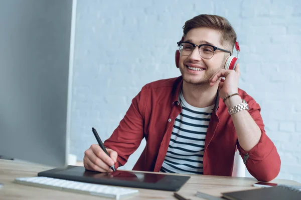 Designer sorridente sentado à mesa com tablet gráfico e computador — Fotografia de Stock