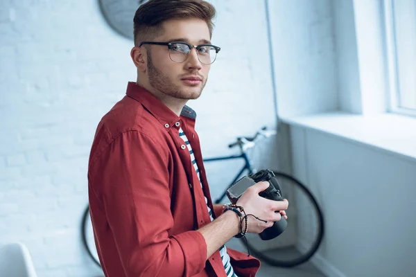 Jeune photographe tenant un appareil photo numérique dans un bureau léger — Photo de stock