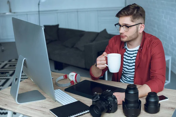 Joven diseñador trabajando por computadora y bebiendo café - foto de stock