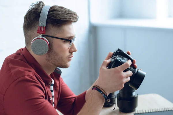 Young bearded man in headphones holding camera by table — Stock Photo