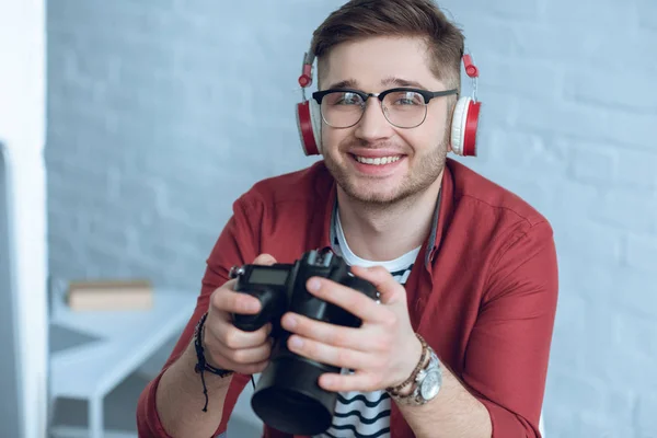 Homme freelance au travail tenant appareil photo numérique dans le bureau de lumière — Photo de stock