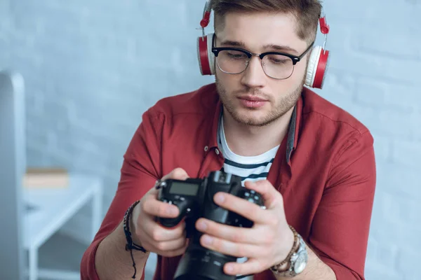 Jeune photographe tenant un appareil photo numérique dans un bureau léger — Photo de stock