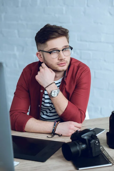 Thoughtful photographer by table with camera and computer — Stock Photo