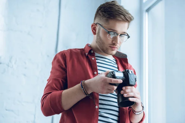 Молодий фотограф дивиться на цифрову камеру в легкому офісі — стокове фото