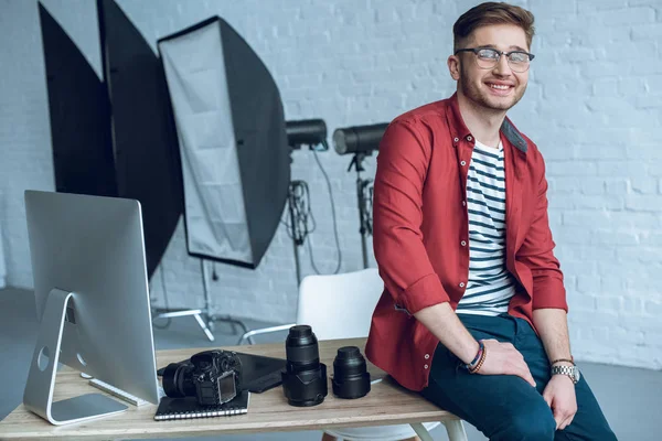 Smiling photographer sitting on table with camera and computer — Stock Photo