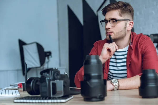 Thoughtful freelancer working by table with camera — Stock Photo