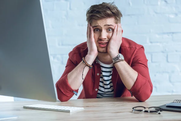 Hombre estresado sentado junto a una mesa de trabajo con computadora - foto de stock