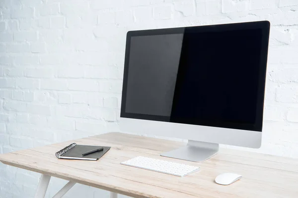 Blank computer screen with notebook on table in light office — Stock Photo