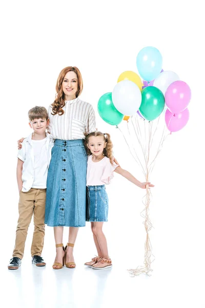 Feliz madre y dos niños con globos de colores de pie juntos y sonriendo a la cámara aislada en blanco - foto de stock