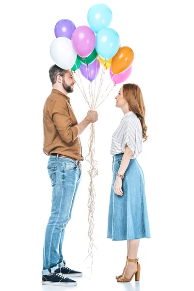 Vista lateral de pareja con globos de colores mirándose aislados en blanco - foto de stock