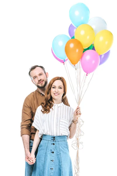 Счастливая пара с красочными воздушными шарами улыбаясь в камеру изолированы на белом — стоковое фото