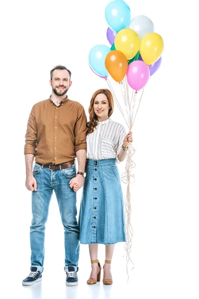 Casal feliz com balões coloridos de mãos dadas e sorrindo para a câmera isolada no branco — Fotografia de Stock