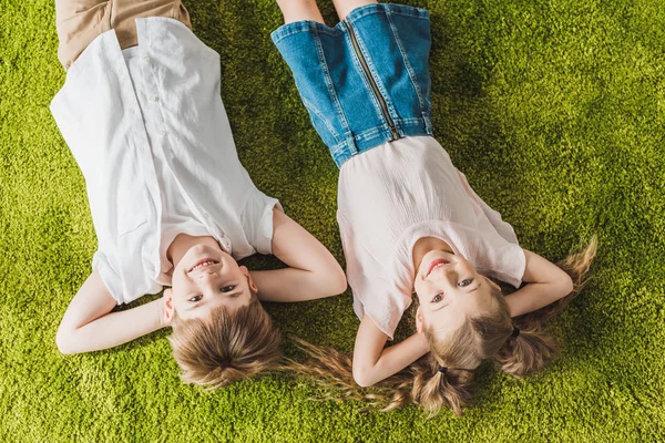 Top view of happy children lying on lawn and smiling at camera — Stock Photo