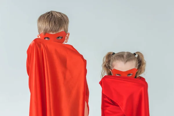 Enfants en masques couvrant les visages avec des manteaux et regardant la caméra isolée sur gris — Photo de stock