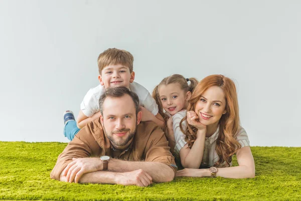 Famille joyeuse avec deux enfants allongés sur la pelouse et souriant à la caméra sur gris — Photo de stock