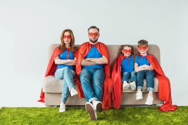 Family in superhero costumes sitting with crossed arms and looking at camera on grey — Stock Photo