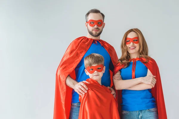 Familia de superhéroes con máscaras y capas mirando a la cámara aislada en gris - foto de stock