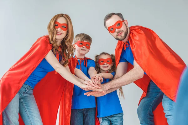 Super family in masks and cloaks stacking hands together isolated on grey — Stock Photo