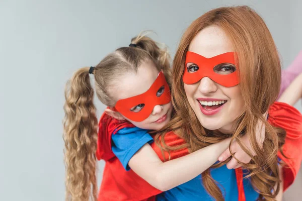 Heureux mère et fille en costumes de super-héros s'amuser ensemble isolé sur gris — Photo de stock
