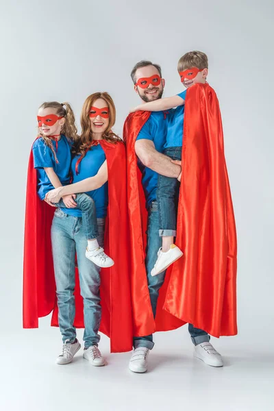 Familia alegre de superhéroes sonriendo a la cámara en gris - foto de stock