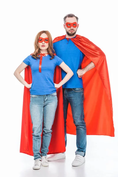 Super couple in masks and cloaks standing with hands on waist and looking at camera isolated on white — Stock Photo