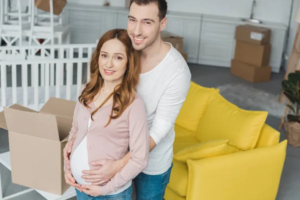 Visão de alto ângulo de feliz casal grávida sorrindo para a câmera no novo apartamento — Fotografia de Stock
