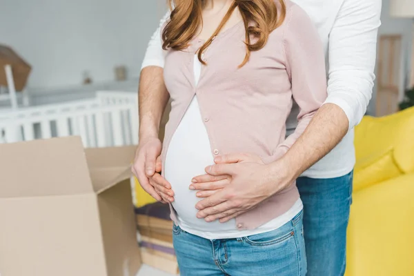 Sección media del hombre abrazando a la esposa embarazada en un nuevo hogar - foto de stock