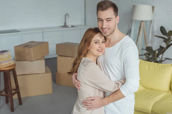 Happy young couple hugging and smiling at camera during relocation — Stock Photo