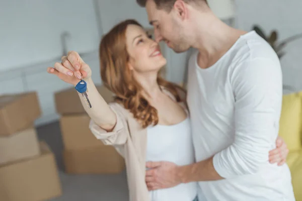 Счастливая молодая пара держит ключи от новой квартиры и улыбается друг другу — стоковое фото