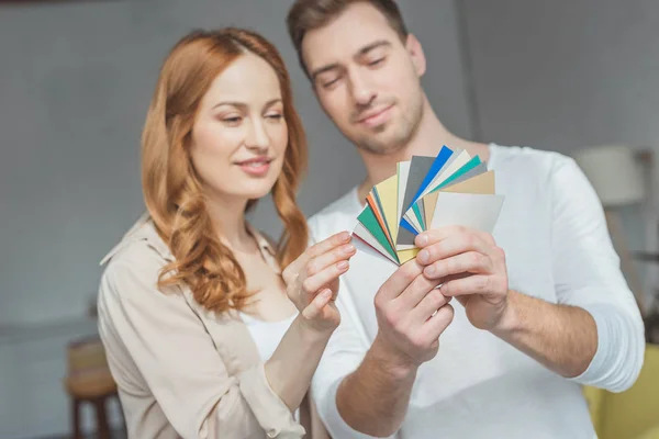 Sonriente pareja joven mirando a la paleta y recogiendo color durante la renovación del apartamento - foto de stock