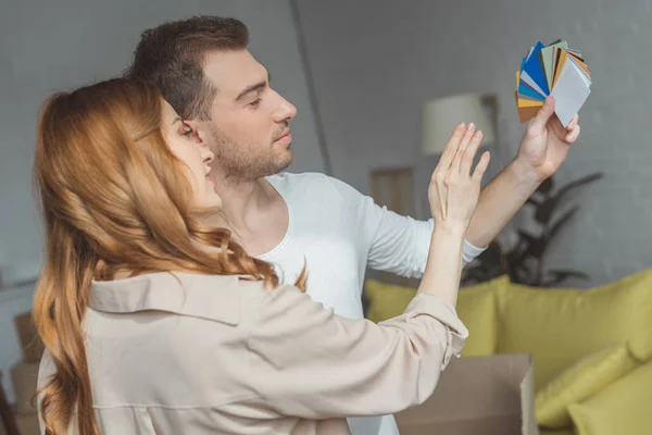 Vista lateral do jovem casal olhando para a paleta e escolhendo a cor ao renovar apartamento — Fotografia de Stock