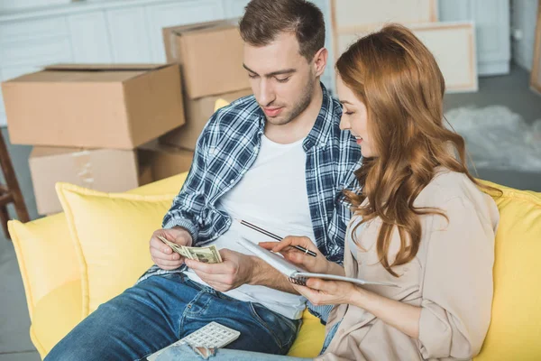 Young couple taking notes and counting money while moving home — Stock Photo