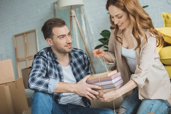 Feliz joven pareja embalaje libros mientras se muda a casa - foto de stock