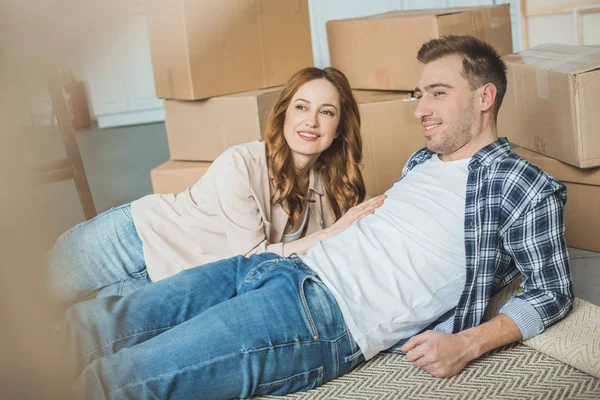 Heureux jeune couple regardant loin tout en emballant des boîtes et déménageant à la maison — Photo de stock