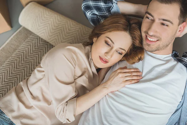 Happy young couple lying on rolled carpet while moving home — Stock Photo