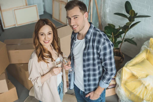 Couple holding glasses of champagne and smiling at camera while celebrating relocation — Stock Photo