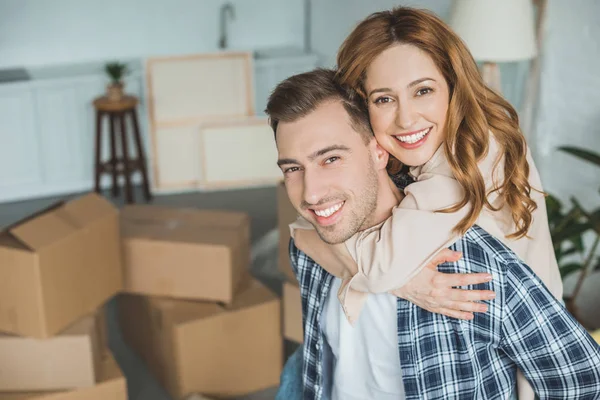 Retrato de esposa feliz abraçando marido em nova casa com caixas de papelão, conceito de realocação — Fotografia de Stock