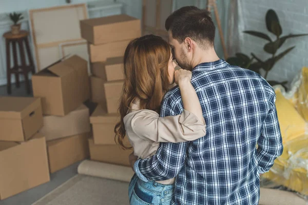 Back view of couple hugging at new apartment full of cardboard boxes, moving home concept — Stock Photo
