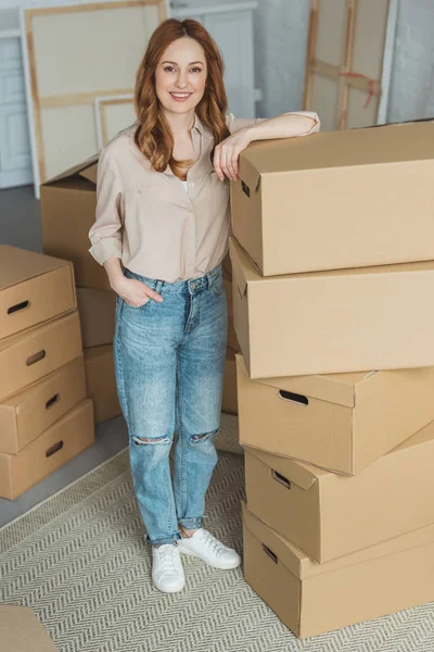 Séduisante femme souriante penchée sur des boîtes en carton dans un nouvel appartement, concept de déménagement — Photo de stock