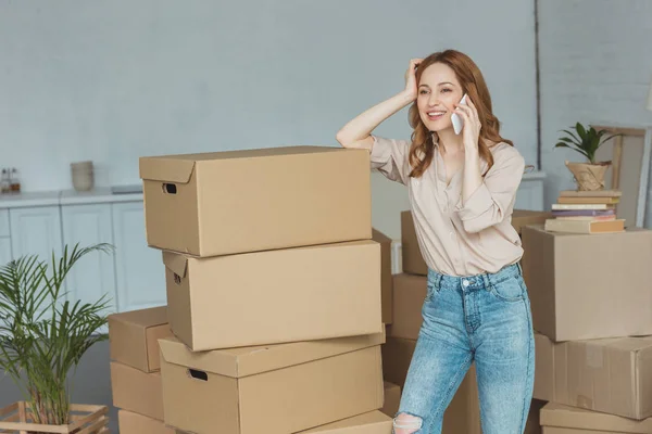 Femme souriante parlant sur smartphone dans un nouvel appartement, concept de relocalisation — Photo de stock