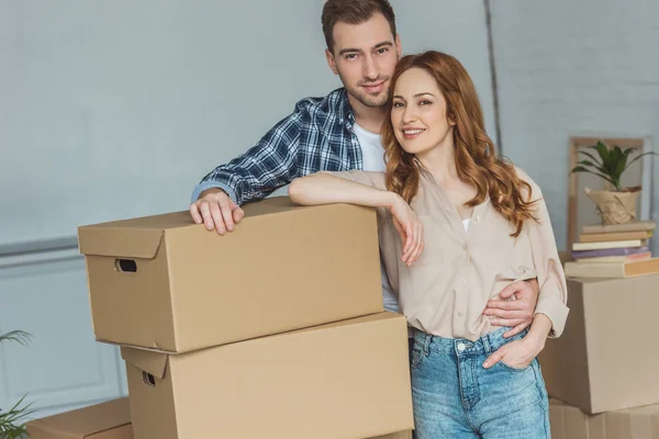 Sorrindo casal inclinando-se sobre pilha de caixas de papelão em nova casa, conceito de realocação — Fotografia de Stock