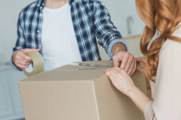 Cropped shot of couple packing cardboard box with sticky tape together, relocation concept — Stock Photo