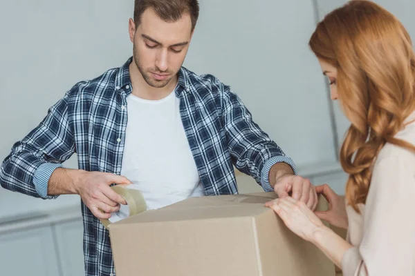 Couple packing cardboard box with sticky tape together, relocation concept — Stock Photo