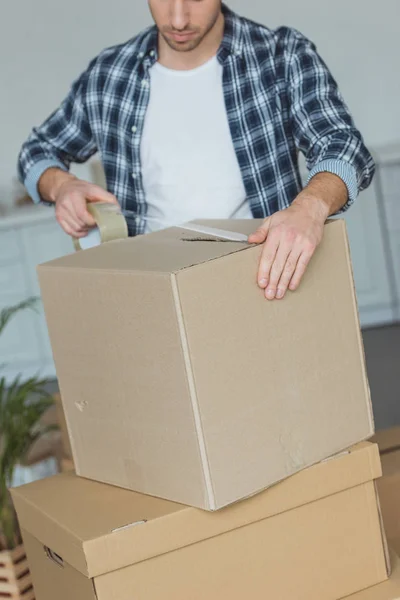 Частичный вид человека упаковки картонной коробки с липкой лентой, концепция перемещения — стоковое фото