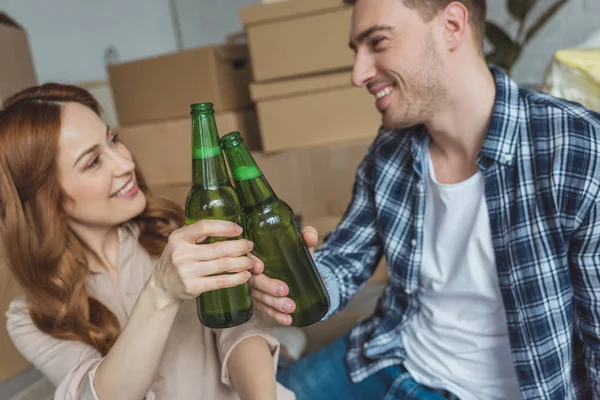 Young couple clinking bottles of beer at new apartment, relocation concept — Stock Photo