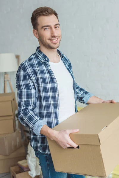 Homme souriant avec boîte en carton dans les mains à la nouvelle maison, concept de relocalisation — Photo de stock