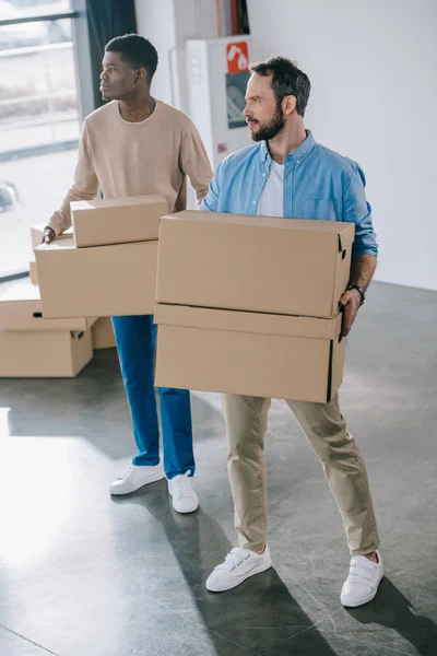 Vista de ángulo alto de los hombres jóvenes multiétnicos que sostienen cajas de cartón durante la reubicación - foto de stock