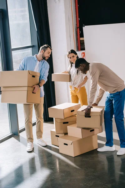 Vista de ángulo alto de los jóvenes multiétnicos que sostienen cajas de cartón durante la reubicación - foto de stock