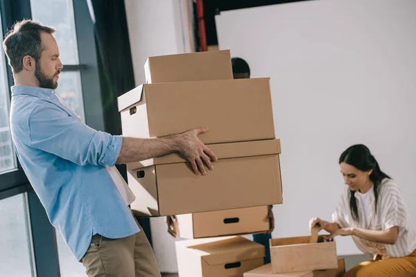 Seitenansicht eines bärtigen Geschäftsmannes, der Kartons in seinem neuen Büro trägt — Stockfoto